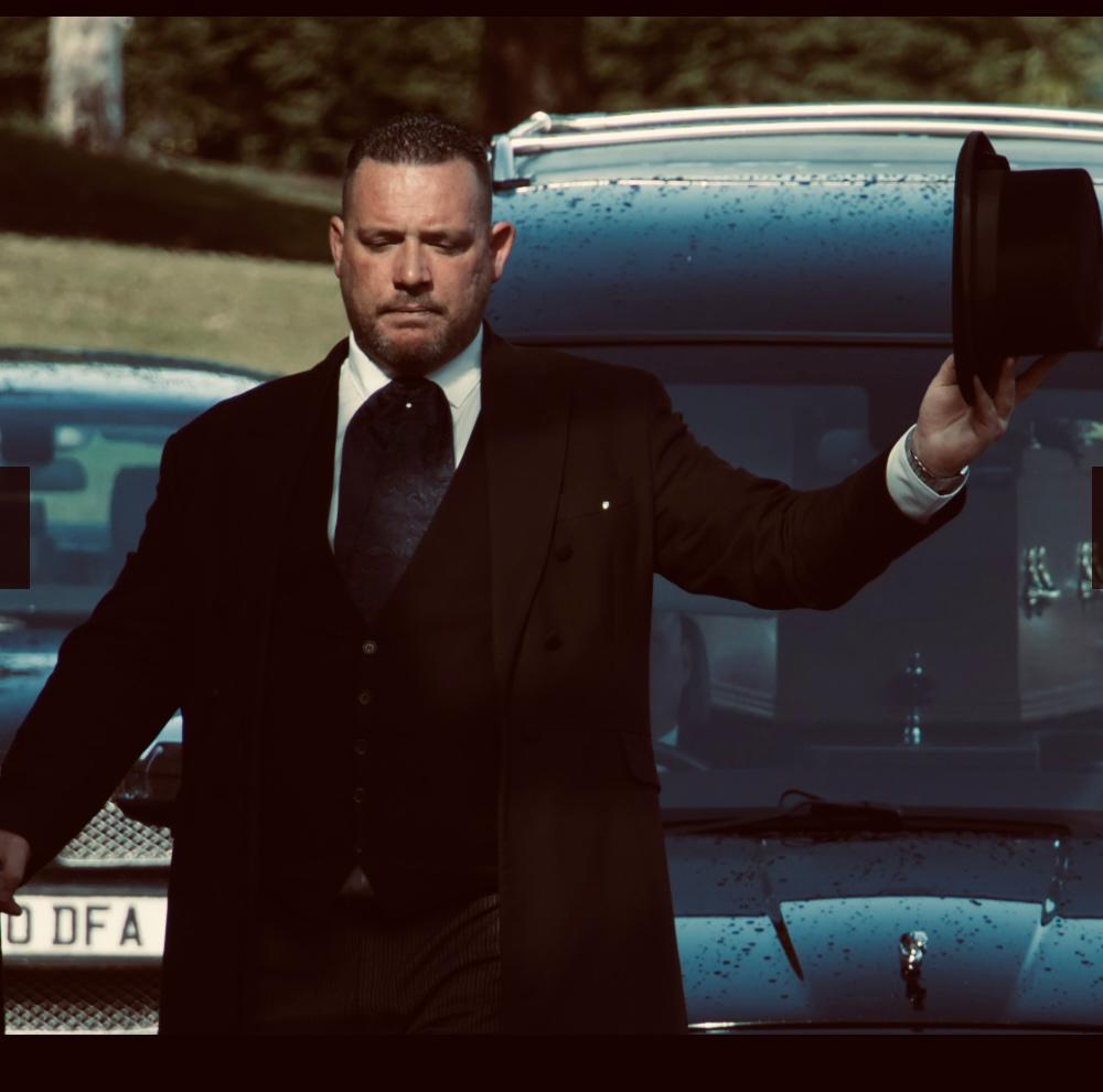 Mathew K Sutton, independent funeral director in Kent, holding his top hat beside a hearse